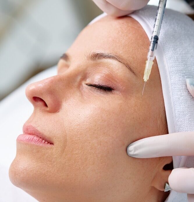 Person receiving a Botox injection on the forehead, eyes closed, wearing a headband, with gloved hands administering the proc