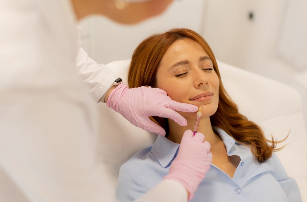 Woman receiving facial injection from professional wearing pink gloves.