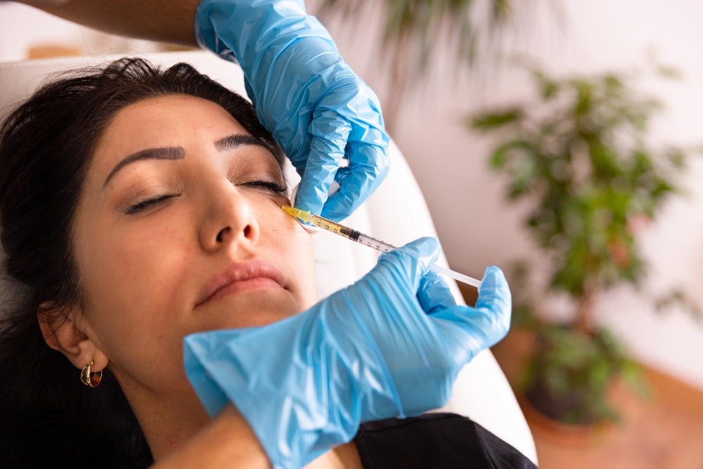 Person receiving Sculptra injection in cheek by gloved hands in a clinical setting.