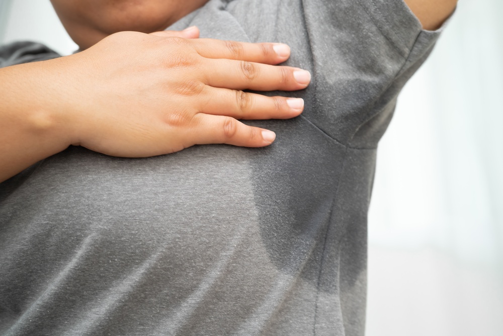 Person touching armpit with visible sweat stain on gray shirt.